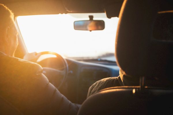 Two people are in a car, driving towards the setting sun.