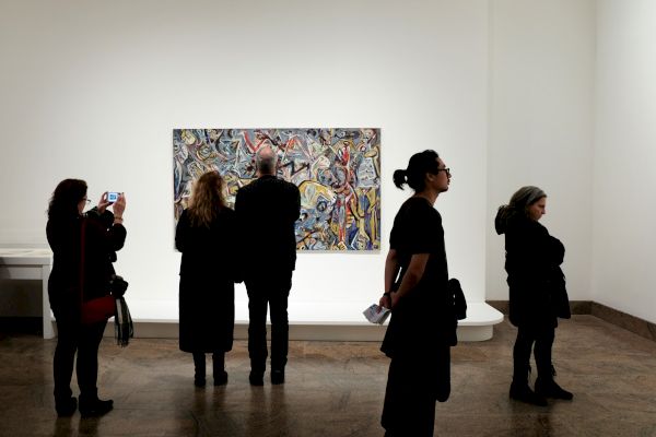 People viewing an abstract painting on a white wall in an art gallery.